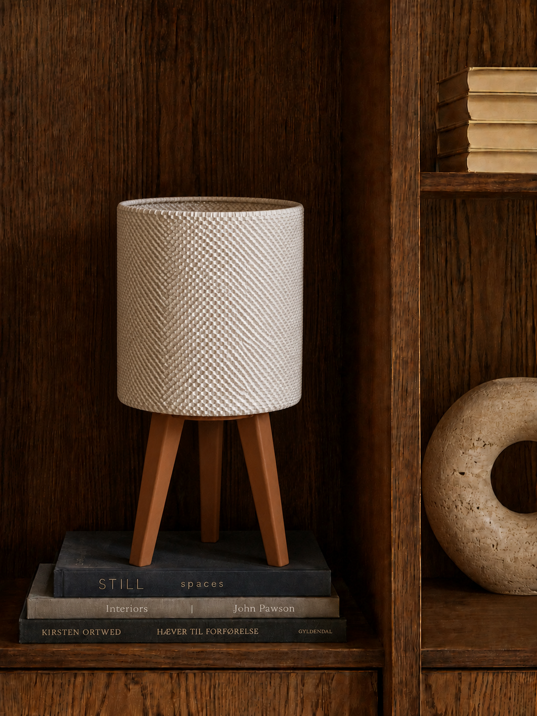 Kete lattice table lamp glowing on a dark wooden bookcase beside books and a stone ring, LAYR, made in New Zealand