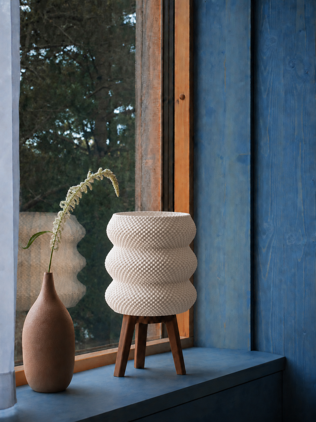 Tai sculptural table lamp in matte white on a windowsill beside a terracotta vase, against a blue wall, LAYR, made in New Zealand